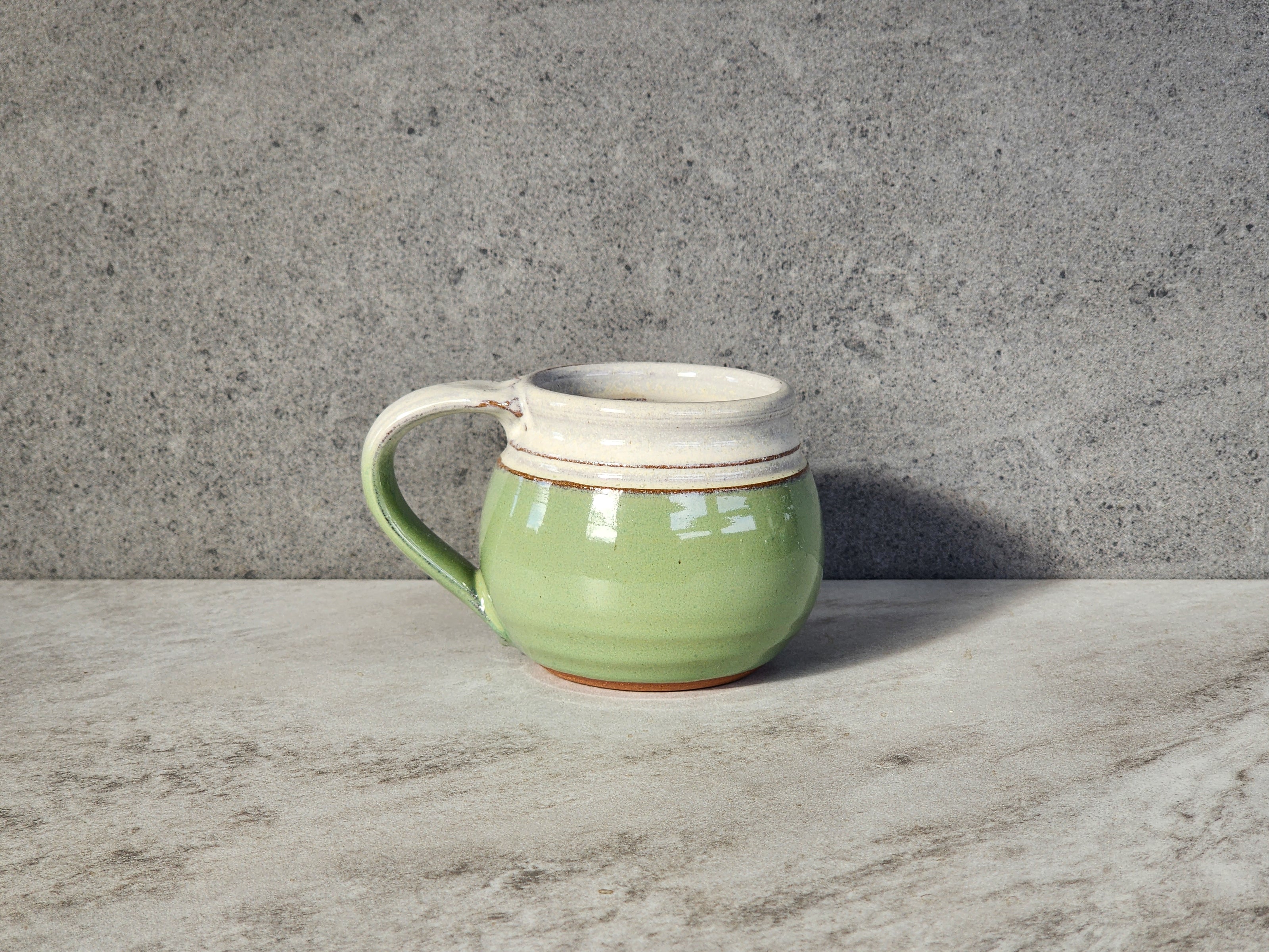 Bud green small mug from Clinton Pottery offers a delightful touch of natural beauty. Its smooth ceramic surface evokes the freshness of spring, while the comfortable handle ensures easy handling. With a capacity of 10-12 ounces, it's ideal for savoring your favorite hot beverages, whether it's a steaming cup of coffee, soothing tea, or rich hot cocoa.