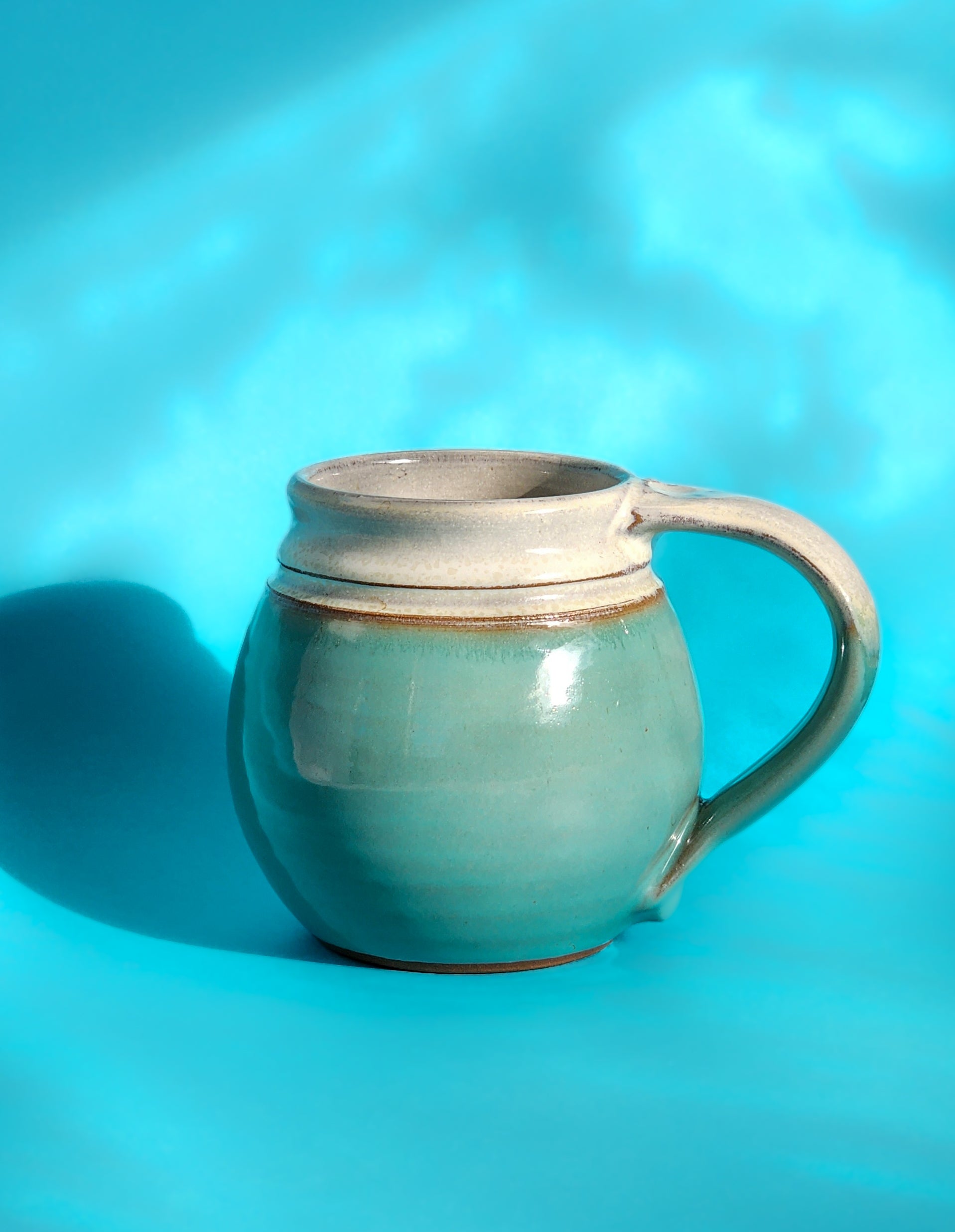 Image: Clinton Pottery's Handmade Medium Mug in Sky Blue – A serene and versatile 14-16 oz mug, expertly crafted. This Sky Blue piece adds a touch of tranquility to your daily beverage routine, reminiscent of clear skies and calm waters. Ideal for savoring moderate quantities of your favorite drinks, it seamlessly combines style with functionality.