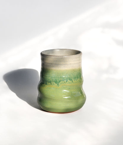 Image: Clinton Pottery's 15 oz Large Tumbler in Bud Green – A visually striking addition with a cool, curvy design for a comfortable grip. This machine washable tumbler, crafted with care, adds contemporary elegance. The refreshing Bud Green color brings a touch of nature's vitality, reminiscent of spring foliage and new beginnings.