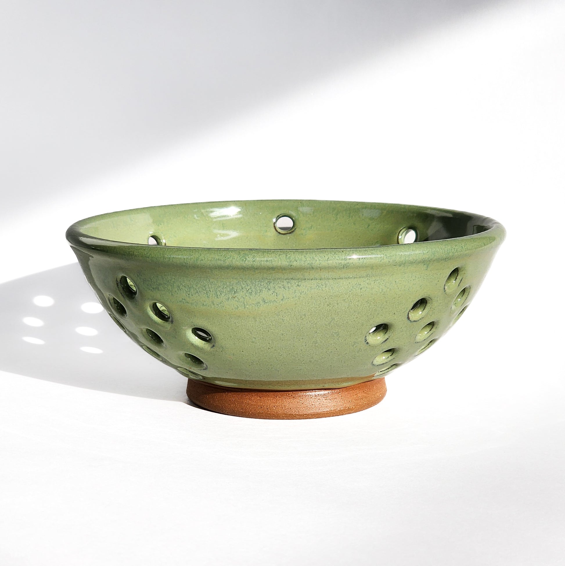 Image: Clinton Pottery's Handmade Medium Colander in Bud Green – A visually appealing and functional kitchen accessory, expertly crafted. This 4 cup colander in refreshing Bud Green is perfect for washing fruits, veggies, or as a stylish counter fruit bowl. Machine washable and seamlessly blending functionality with vibrant charm, it's ideal for those seeking style and practicality.
