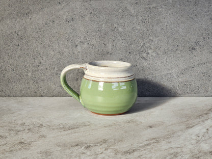  Bud green small mug from Clinton Pottery offers a delightful touch of natural beauty. Its smooth ceramic surface evokes the freshness of spring, while the comfortable handle ensures easy handling. With a capacity of 10-12 ounces, it's ideal for savoring your favorite hot beverages, whether it's a steaming cup of coffee, soothing tea, or rich hot cocoa.
