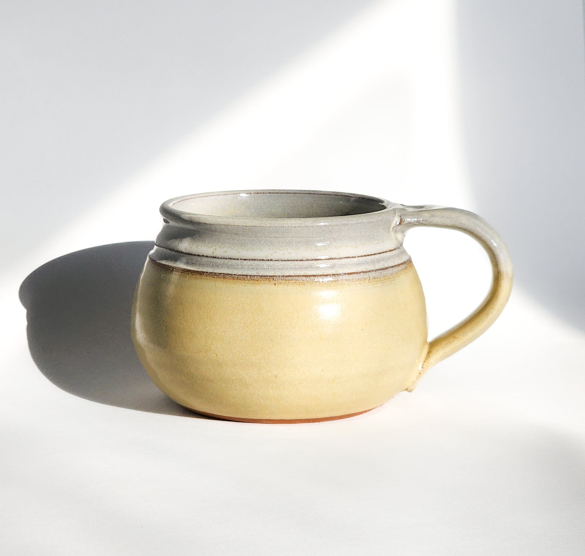 Image: Clinton Pottery's 24 oz Cereal/Soup Mug in Butter Yellow – A warm and inviting addition to your kitchen, this machine washable mug seamlessly blends artistry with functionality. The gentle Butter Yellow color adds a touch of sunshine, reminiscent of golden fields and cozy kitchens. Perfect for savoring your favorite cereal or soup with a dash of comforting charm.