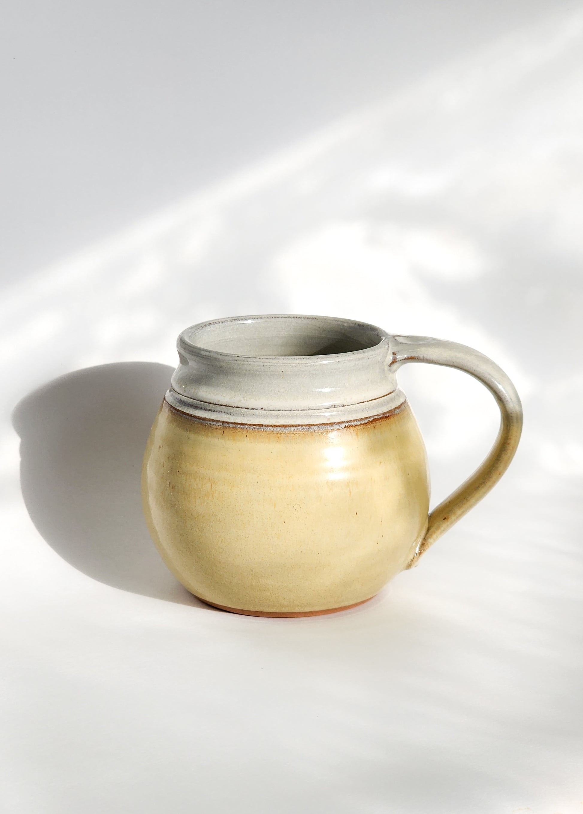  Image: Clinton Pottery's Handmade Medium Mug in Butter Yellow – A cheerful and versatile 14-16 oz mug, expertly crafted. This Butter Yellow piece adds a touch of warmth and sunshine to your daily beverage routine, reminiscent of golden fields and happiness. Ideal for savoring moderate quantities of your favorite drinks, it seamlessly combines vibrant style with functionality. The soft yellow hue enhances the cheerful appeal of this medium-sized mug. 