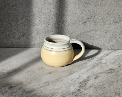 Clinton Pottery's Butter Yellow small mug, sized at 10-12 oz, radiates warmth and charm, perfect for brightening any moment. Crafted with care, it boasts a smooth surface and comfortable handle, making it a pleasure to hold. Ideal for your favorite hot beverages, it adds a touch of cozy elegance to your daily routine. Embrace the comfort and joy of sipping from this delightful Butter Yellow mug, a perfect addition to your collection.