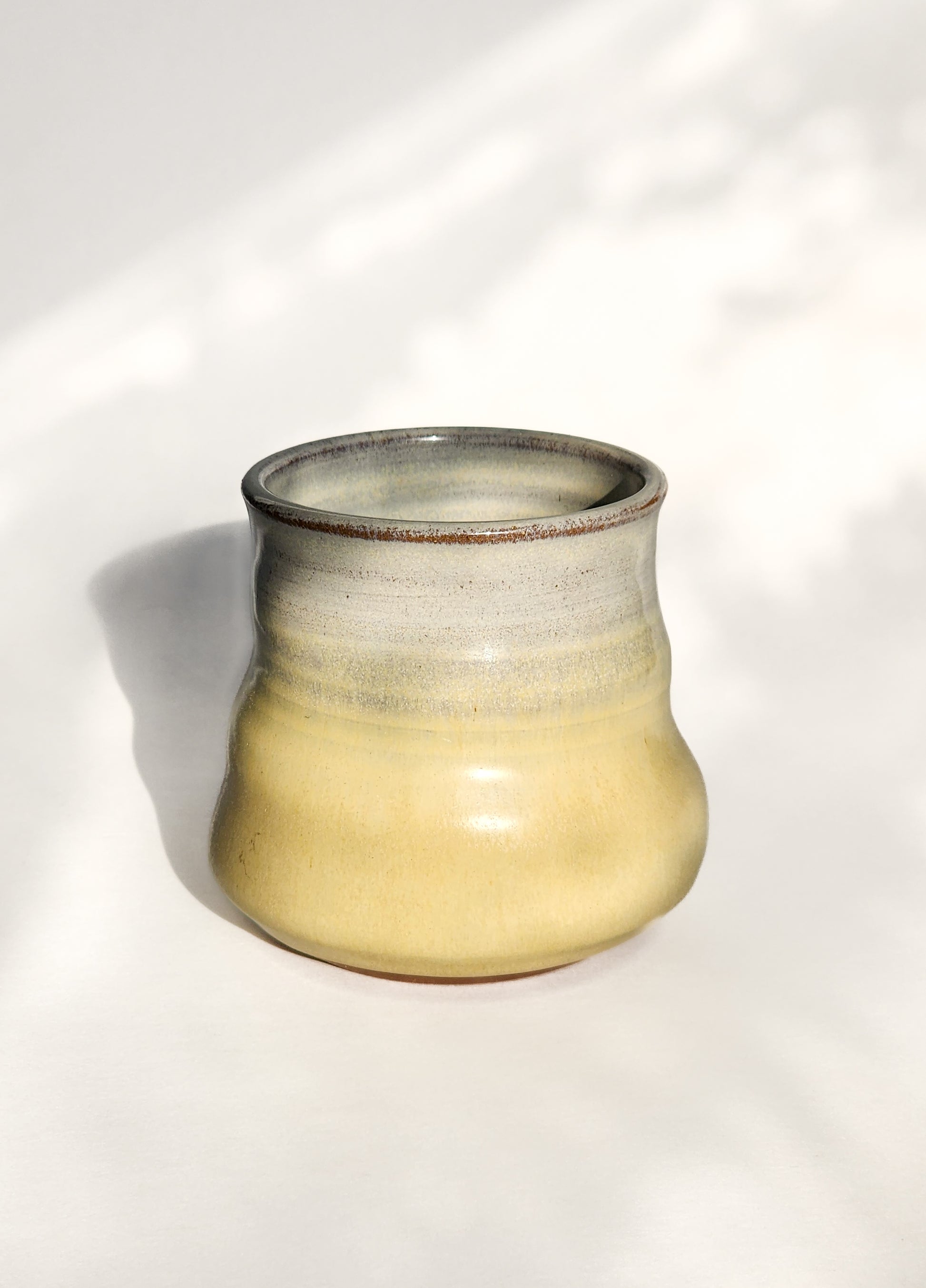 Image: Clinton Pottery's 8 oz Small Tumbler in Butter Yellow – A visually appealing addition with a cool, curvy design for a comfortable grip. This machine washable tumbler, crafted with care, adds contemporary elegance. The gentle Butter Yellow color brings warmth, reminiscent of golden fields and cozy kitchens.