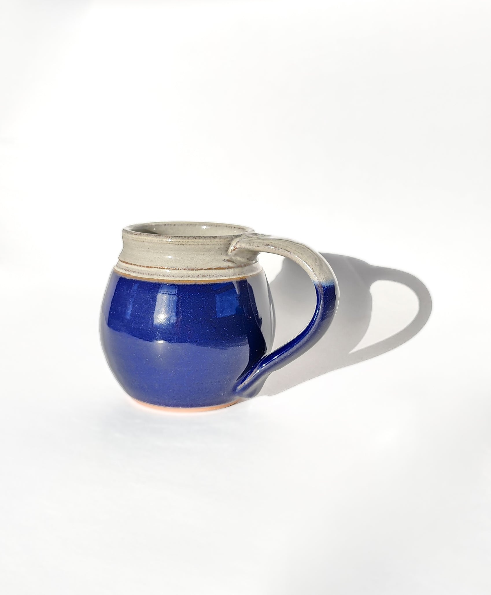  Image: Clinton Pottery's Handmade Medium Mug in Cobalt Blue – A bold and versatile 14-16 oz mug, expertly crafted. This Cobalt Blue piece adds a splash of vibrant elegance to your daily beverage routine, reminiscent of deep ocean waters and sophistication. Ideal for savoring moderate quantities of your favorite drinks, it seamlessly combines style with functionality. The rich cobalt blue hue enhances the bold appeal of this medium-sized mug.