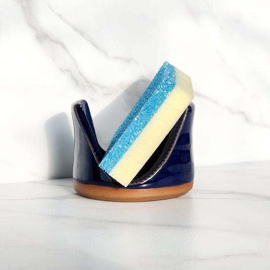 Image: Clinton Pottery's Handmade Sponge Holder in Cobalt Blue – A bold and practical kitchen accessory, meticulously crafted by artisans. This durable stoneware holder, in striking Cobalt Blue, adds a touch of vibrant sophistication to your kitchen, reminiscent of deep blue ocean depths and timeless elegance. Designed to securely hold your sponge and prevent water spread, it keeps your counters and sink area tidy. 
