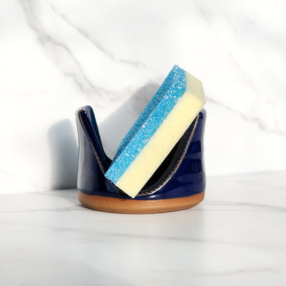 Image: Clinton Pottery's Handmade Sponge Holder in Cobalt Blue – A bold and practical kitchen accessory, meticulously crafted by artisans. This durable stoneware holder, in striking Cobalt Blue, adds a touch of vibrant sophistication to your kitchen, reminiscent of deep blue ocean depths and timeless elegance. Designed to securely hold your sponge and prevent water spread, it keeps your counters and sink area tidy. 