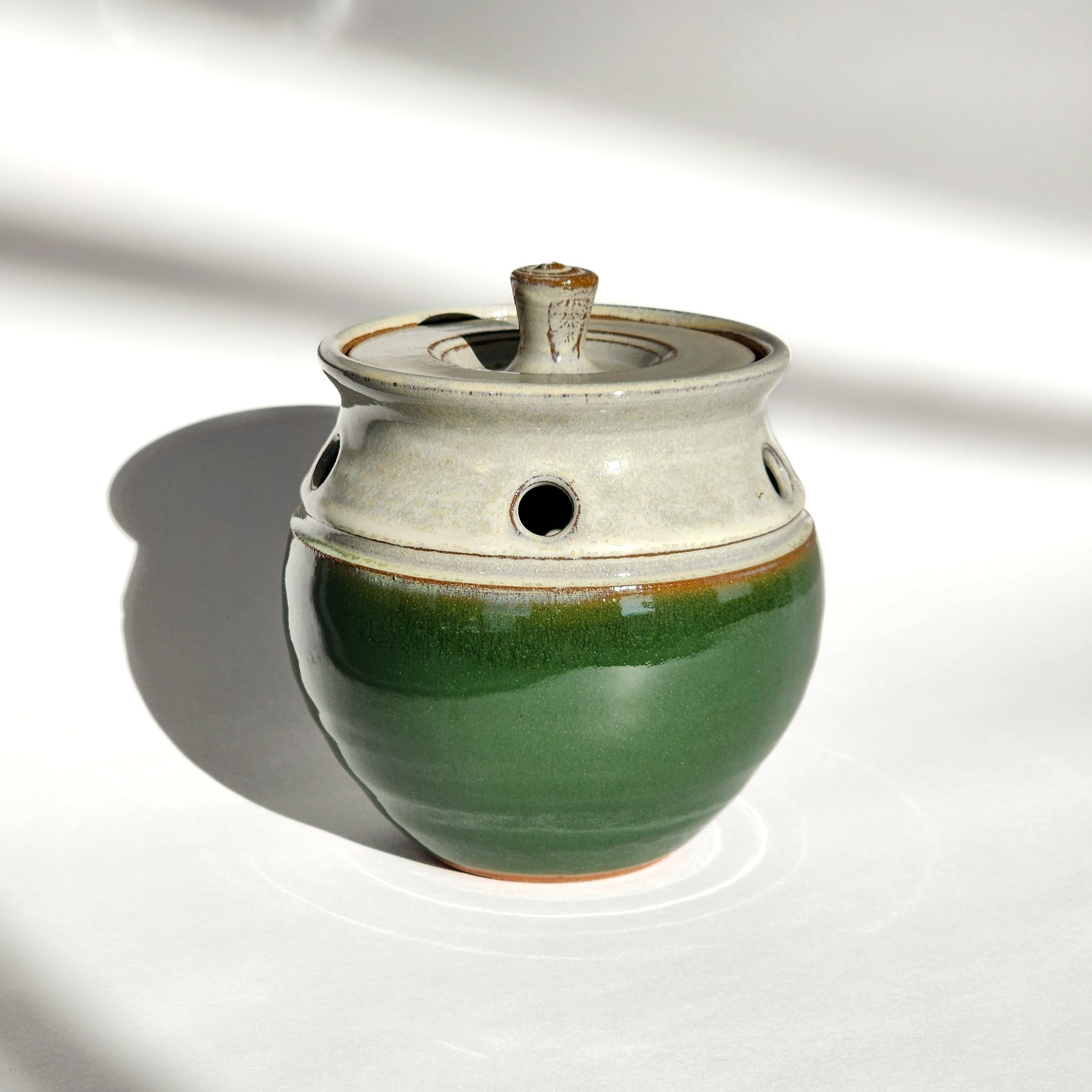 Image: A dark green ceramic garlic keeper, crafted to store garlic bulbs and keep them fresh for longer.