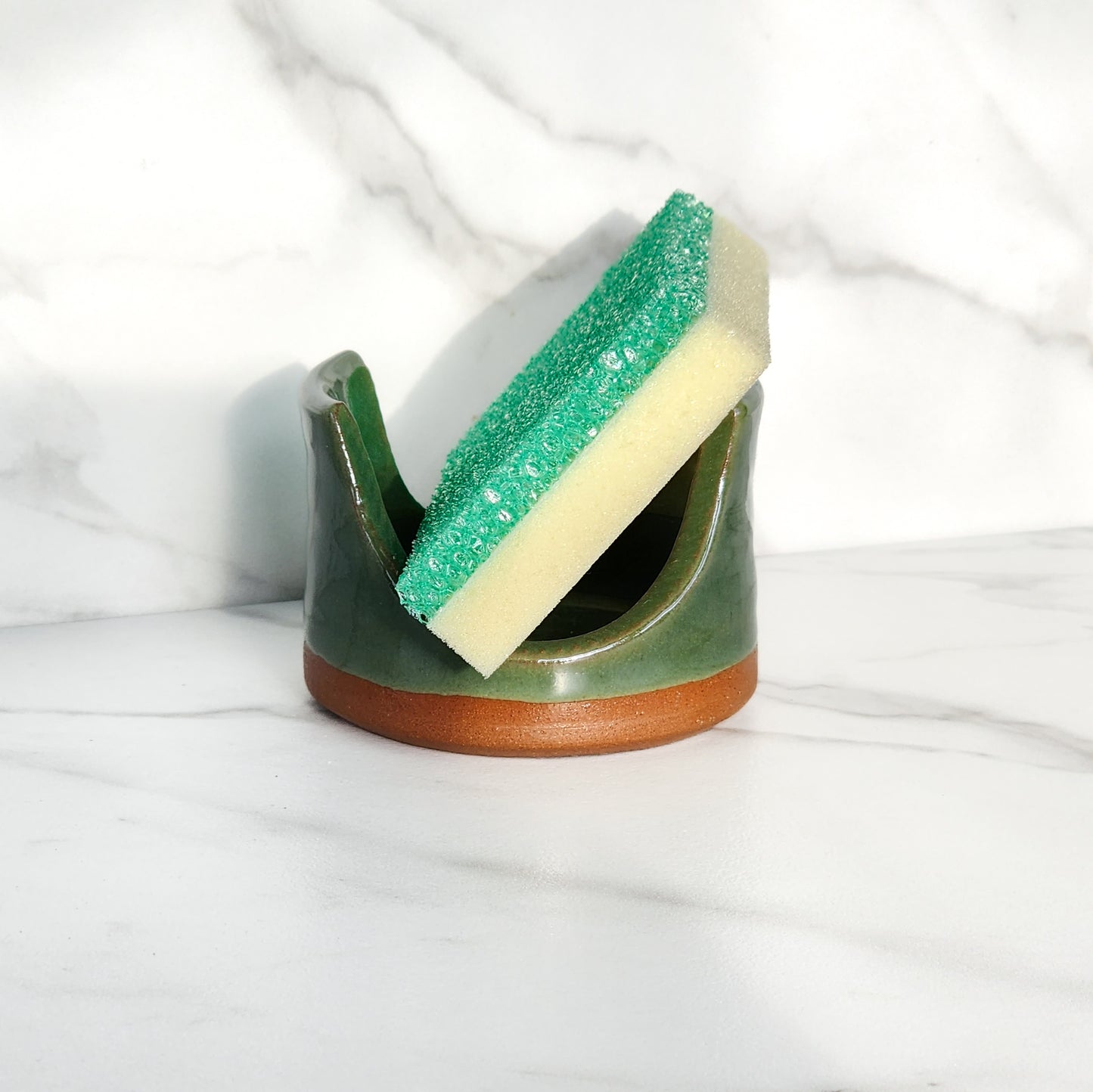 Image: Clinton Pottery's Handmade Sponge Holder in Dark Green – A rich and practical kitchen accessory, skillfully crafted by artisans. This durable stoneware holder, in deep Dark Green, brings a sense of natural elegance to your kitchen, reminiscent of lush forests and tranquility. Designed to securely hold your sponge and prevent water spread, it keeps your counters and sink area tidy.