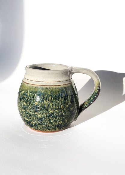  Image: Clinton Pottery's Handmade Jumbo Mug in Froggy Bottom – A whimsical and generously sized 30 oz mug, expertly crafted. This Froggy Bottom piece adds a touch of playful charm to your daily beverage routine, reminiscent of lily pads and pond adventures. Ideal for savoring larger quantities of your favorite drinks, it seamlessly combines style with functionality. The earthy green hue enhances the delightful appeal of this substantial mug. 