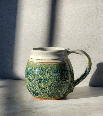 Image: Clinton Pottery's Medium Mug in Froggy Bottom – A charming 14-16 oz mug, expertly crafted. This Froggy Bottom piece adds whimsy to your routine, reminiscent of pond adventures. Ideal for savoring moderate quantities of your favorite drinks, it seamlessly combines style with functionality. The earthy green hue enhances the delightful appeal of this medium-sized mug. Machine washable for convenience, it's an ideal choice for those who appreciate whimsical aesthetics and practicality.
