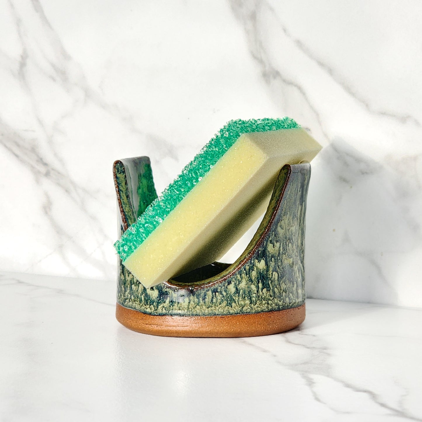 Image: Clinton Pottery's Handmade Sponge Holder in Froggy Bottom – A whimsical and practical kitchen accessory, expertly crafted by artisans. This durable stoneware holder, in playful Froggy Bottom, adds a touch of lighthearted charm to your kitchen, reminiscent of outdoor adventures and cheerful nature. Designed to securely hold your sponge and prevent water spread, it keeps your counters and sink area tidy. 