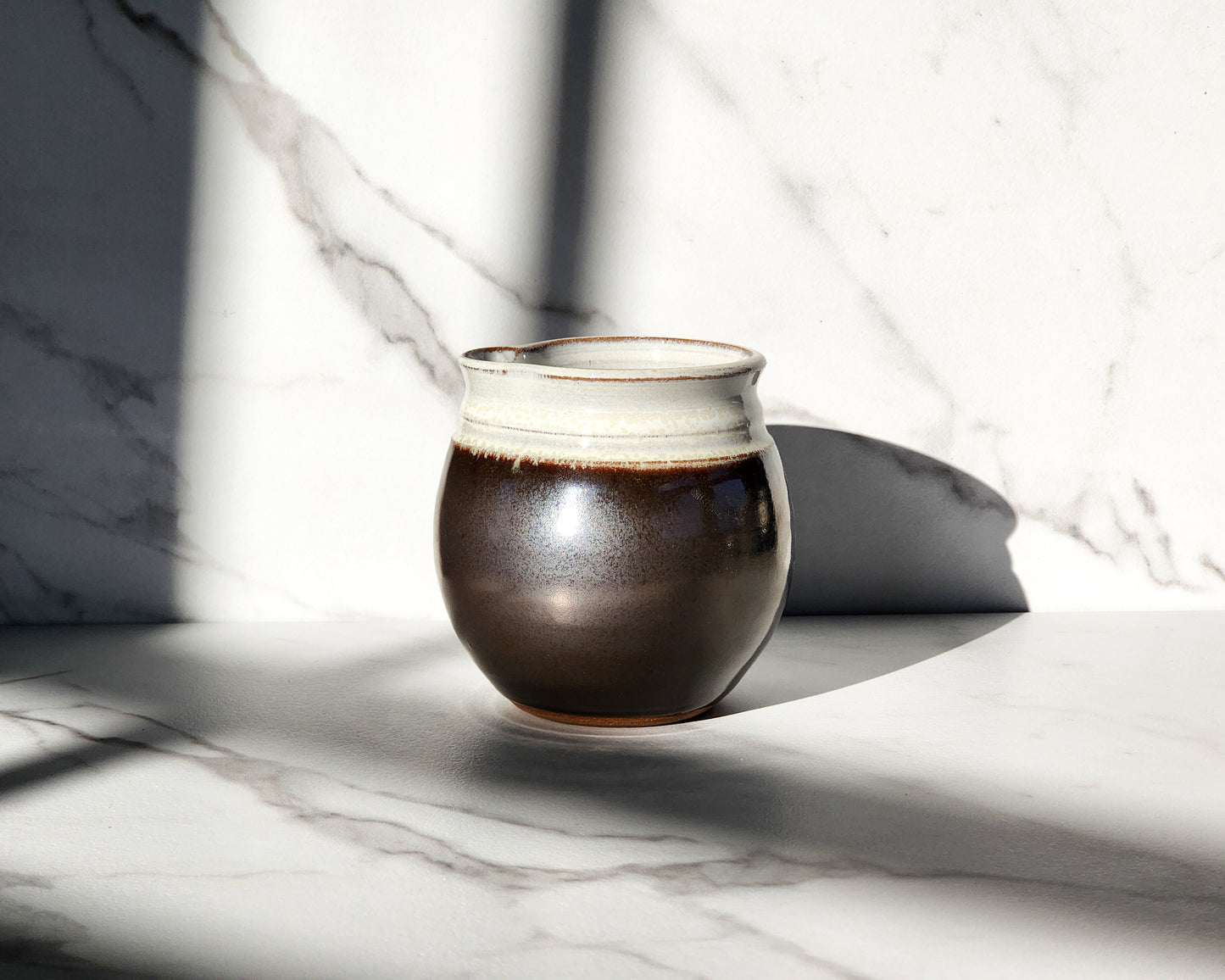  Image Description: A Licorice creamer from Clinton Pottery rests gracefully on a table, its deep black color exuding sophistication and elegance. With its sleek design and smooth finish, this creamer adds a touch of modern refinement to any tabletop. Ideal for serving cream or milk alongside coffee or tea.