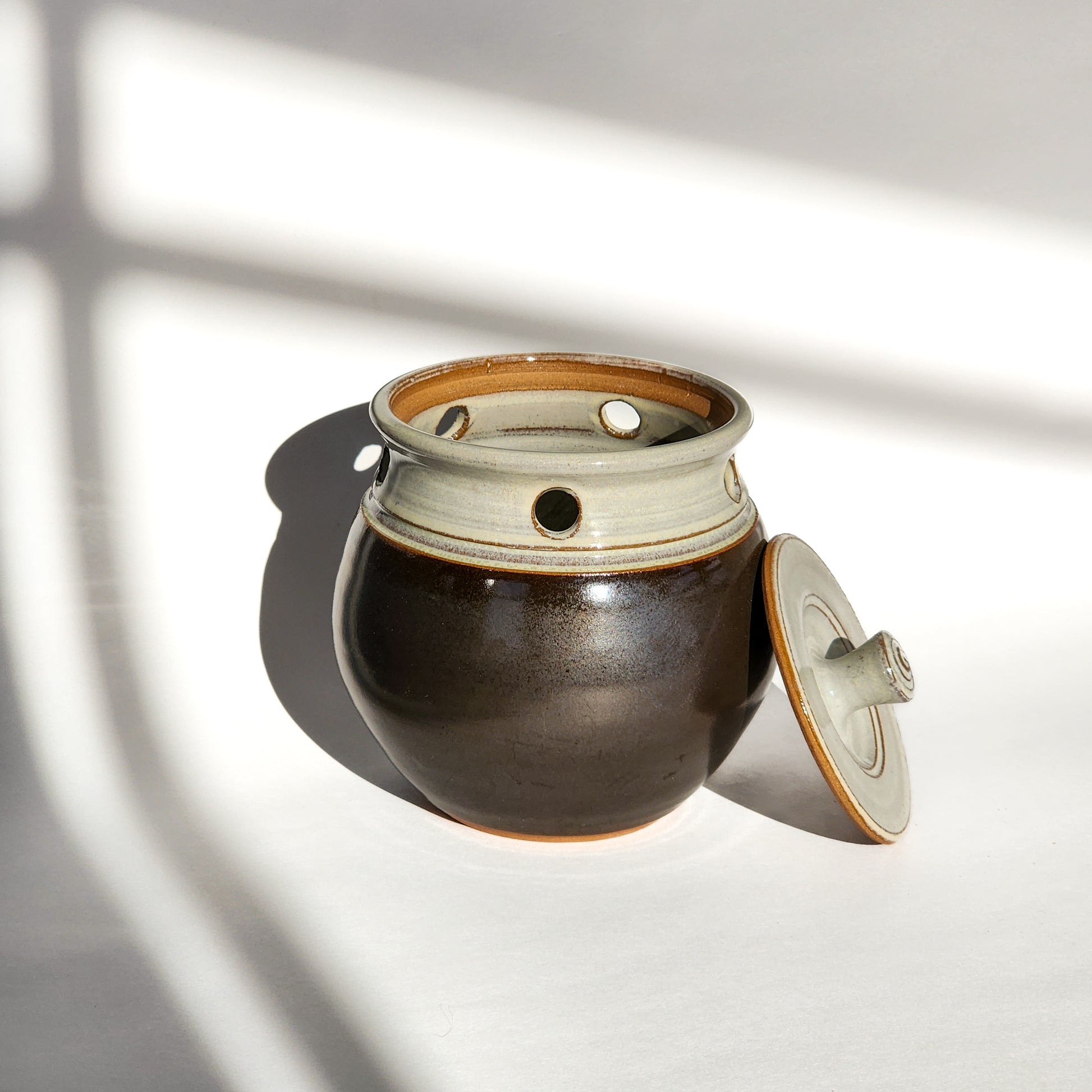 Image: A licorice glazed ceramic garlic keeper, designed to store garlic bulbs and add elegance to any kitchen.