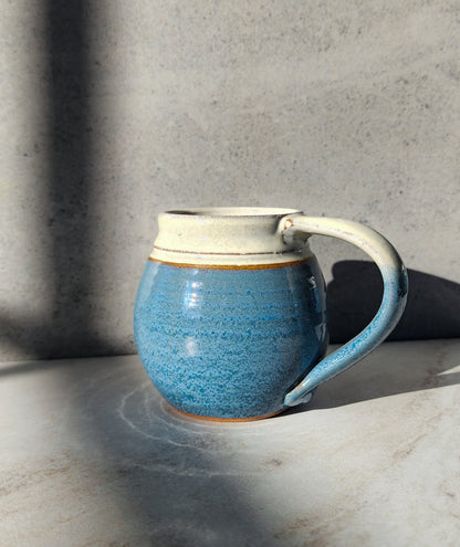 Image: Clinton Pottery's Medium Mug in Light Blue – A serene 14-16 oz mug, expertly crafted. This Light Blue piece adds tranquility to your routine, reminiscent of clear skies. Ideal for savoring moderate quantities of your favorite drinks, it seamlessly combines style with functionality. The soft blue hue enhances the calming appeal of this medium-sized mug. Machine washable for convenience, it's an ideal choice for those who appreciate soothing aesthetics and practicality.