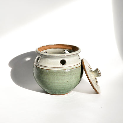 Image: A light green ceramic garlic keeper, crafted to store garlic bulbs and complement kitchen aesthetics.