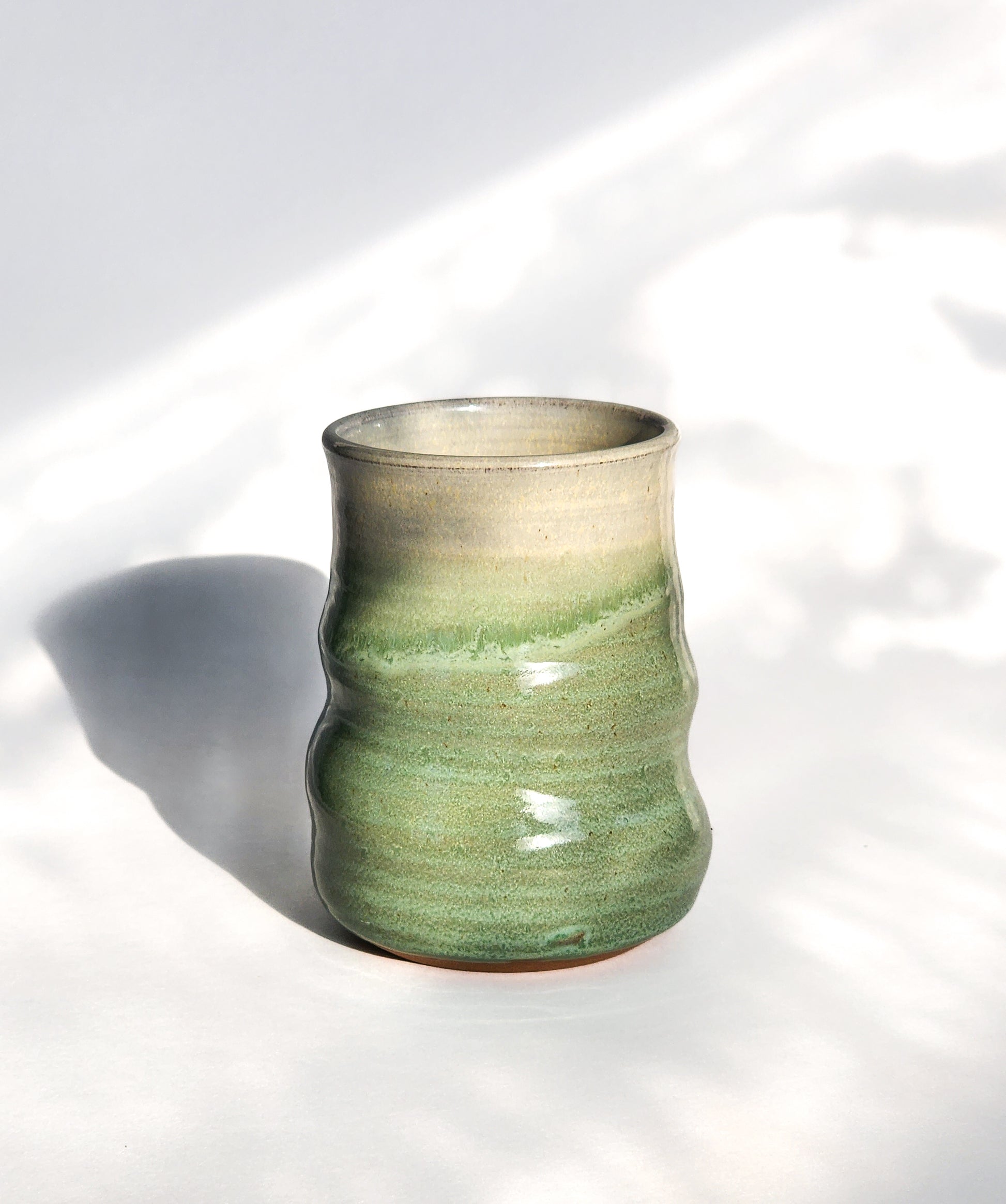 Image: Clinton Pottery's 15 oz Large Tumbler in Light Green – A visually striking addition with a cool, curvy design for a comfortable grip. This machine washable tumbler, crafted with care, adds contemporary elegance. The invigorating Light Green color brings a touch of nature's vitality, reminiscent of spring foliage and sunlit meadows.