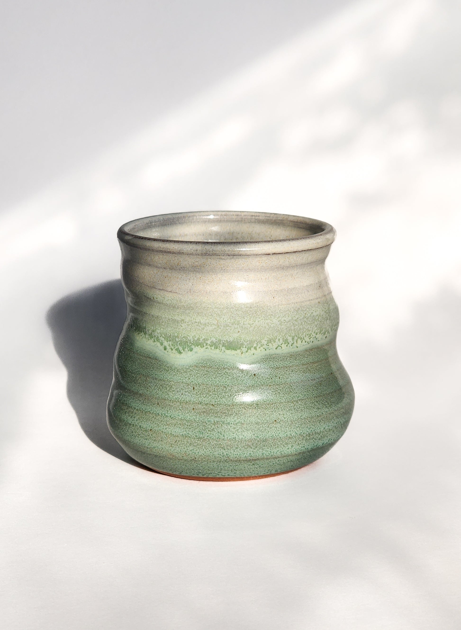 Image: Clinton Pottery's 8 oz Small Tumbler in Light Green – A visually appealing addition with a cool, curvy design for a comfortable grip. This machine washable tumbler, crafted with care, adds contemporary elegance. The invigorating Light Green color brings a touch of nature's vitality, reminiscent of spring foliage and sunlit meadows.