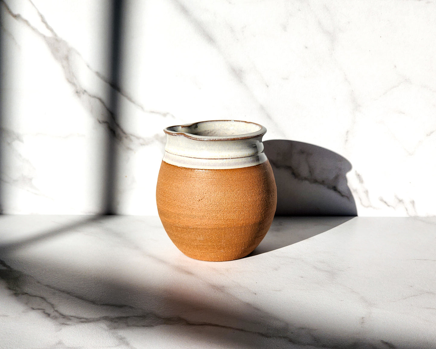 Image Description: A Natural creamer by Clinton Pottery sits elegantly on a table, showcasing its earthy and organic appearance. Crafted with a smooth surface and minimalist design, this creamer exudes a rustic charm that complements any tabletop. Ideal for serving cream or milk alongside coffee or tea.