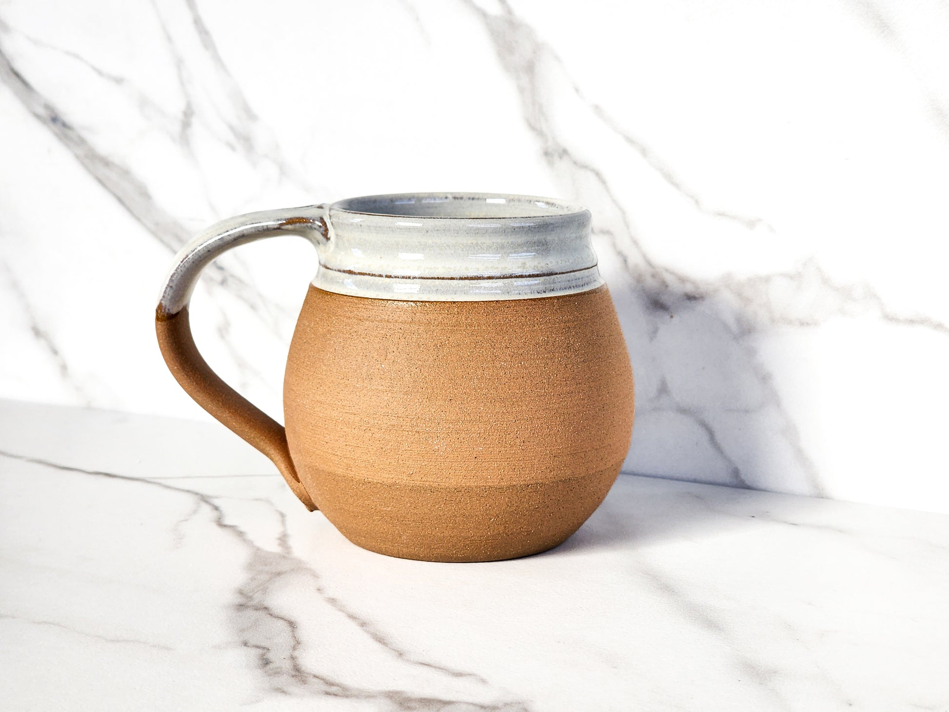 The image depicts a Natural medium mug by Clinton Pottery. Its earthy tone evokes a sense of warmth and tranquility, perfectly complementing the cozy ambiance of a morning coffee ritual.