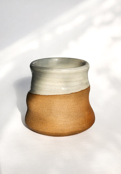 Image: Clinton Pottery's 8 oz Small Tumbler in Natural – A visually appealing addition with a cool, curvy design for a comfortable grip. This machine washable tumbler, crafted with care, adds contemporary elegance. The Natural, unglazed finish brings an earthy and authentic touch, reminiscent of rustic charm and simplicity.