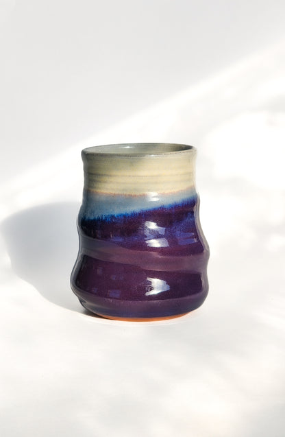 Image: Clinton Pottery's 15 oz Large Tumbler in Purple – A visually striking addition with a cool, curvy design for a comfortable grip. This machine washable tumbler, crafted with care, adds contemporary elegance. The regal Purple color brings a touch of sophistication, reminiscent of royal richness and artistic flair.