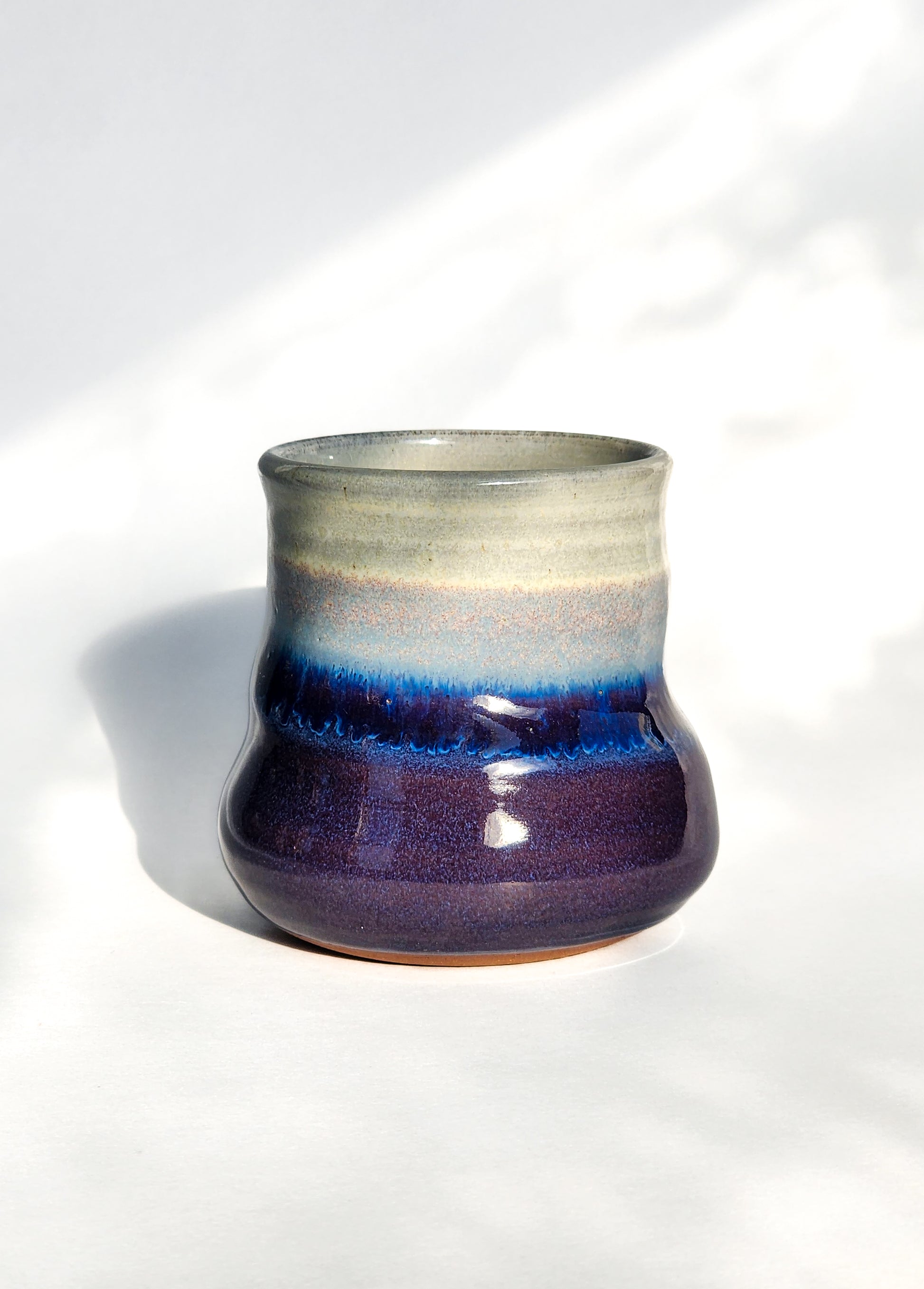 Image: Clinton Pottery's 8 oz Small Tumbler in Purple – A visually appealing addition with a cool, curvy design for a comfortable grip. This machine washable tumbler, crafted with care, adds contemporary elegance. The regal Purple color brings a touch of sophistication, reminiscent of royal richness and artistic flair.