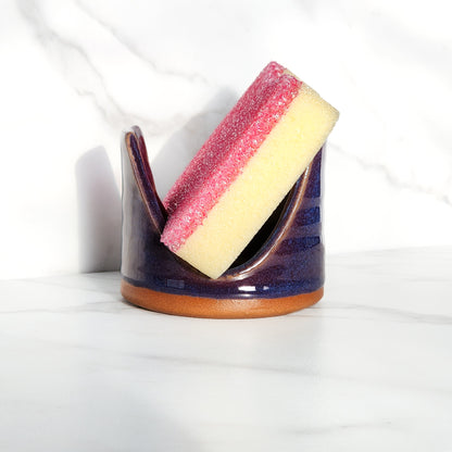  Image: Clinton Pottery's Handmade Sponge Holder in Purple – A regal and practical kitchen accessory, meticulously crafted by artisans. This durable stoneware holder, in rich Purple, adds a touch of sophistication to your kitchen, reminiscent of royal elegance. Designed to securely hold your sponge and prevent water spread, it keeps your counters and sink area tidy.