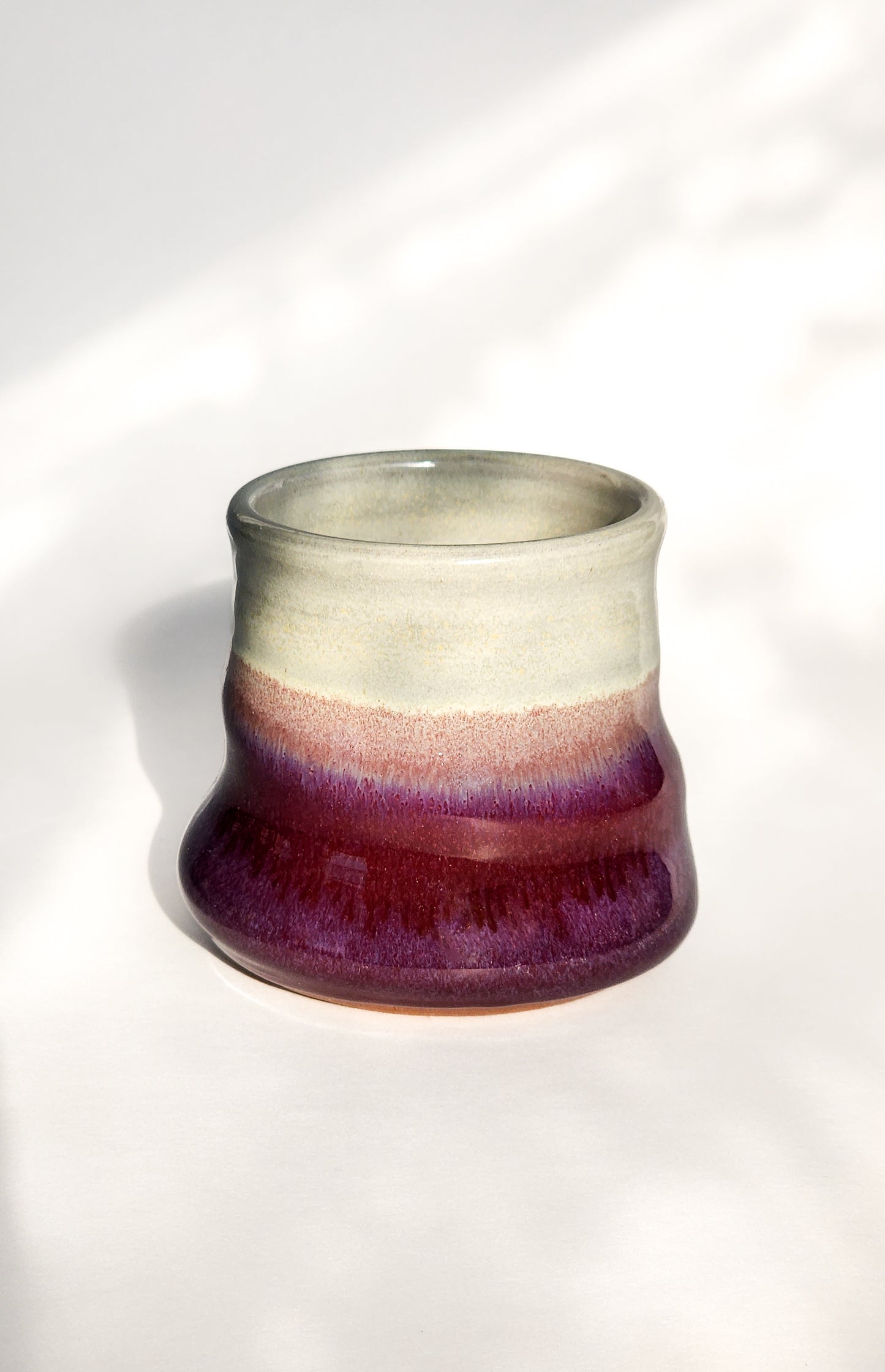Image: Clinton Pottery's 8 oz Small Tumbler in Red/Magenta – A visually appealing addition with a cool, curvy design for a comfortable grip. This machine washable tumbler, crafted with care, adds contemporary elegance. The vibrant Red/Magenta color brings a touch of boldness, reminiscent of passion and artistic expression.
