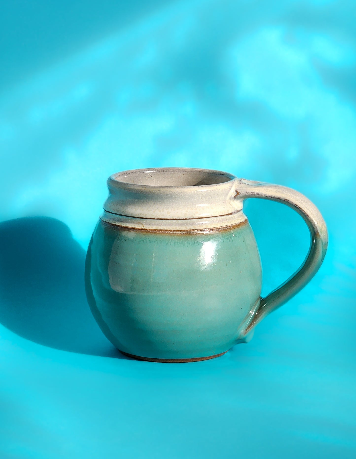Image: Clinton Pottery's Handmade Medium Mug in Sky Blue – A serene and versatile 14-16 oz mug, expertly crafted. This Sky Blue piece adds a touch of tranquility to your daily beverage routine, reminiscent of clear skies and calm waters. Ideal for savoring moderate quantities of your favorite drinks, it seamlessly combines style with functionality. 